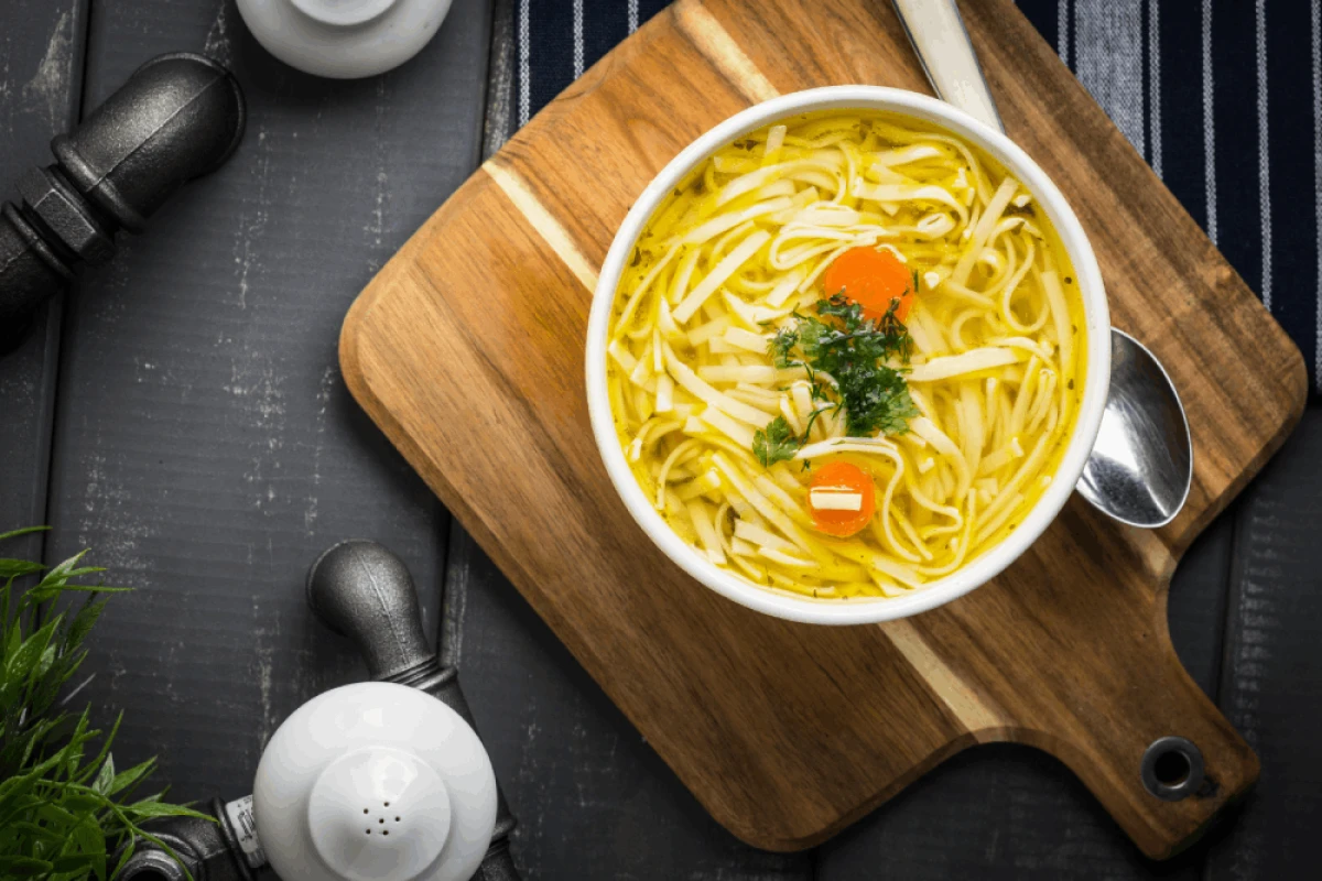 Rosół z makaronem, marchewką i natką pietruszki podany w białej misce